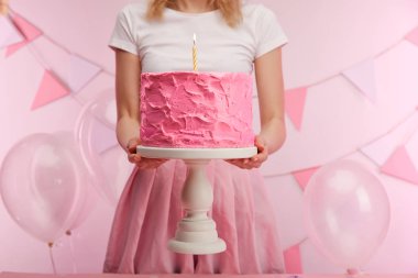 kırpılan görünümünü kek standı tatlı pembe doğum günü pastası ve yakın hava balonları ve dekorasyon yanan mum tutan kadın