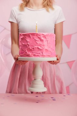 kırpılan görünümünü kek standı tatlı pembe doğum günü pastası ve yanan mum tutan kadın 
