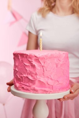 seçici odak kek standı ile lezzetli pembe doğum günü pastası ve yanan mum tutan kadın