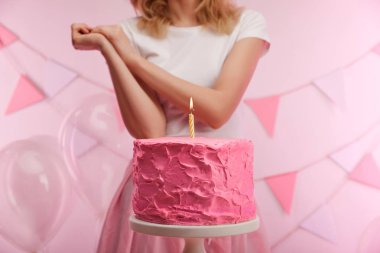 seçici odak kek standı lezzetli pembe doğum günü pastası ve kadın yakınındaki yanan mum ile