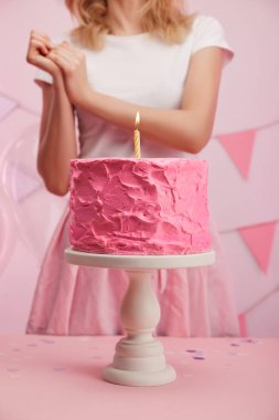 kek standı lezzetli pembe doğum günü pastası ve yanan mum ile yakın duran kadın kırpılmış görünümünü