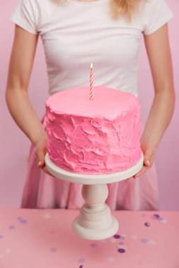 kırpılan görünümünü kek standı tatlı pembe doğum günü pastası ve yanan mum tutan kadın 