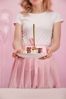 kırpılan görünümünü plaka parça lezzetli doğum günü pastası ve altın çatal ile pembe üzerinde tutan kadın