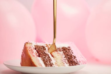doğum günü pastası pembe hava balonları yakınındaki beyaz daire içinde altın çatal ile lezzetli parçasının seçici odak 