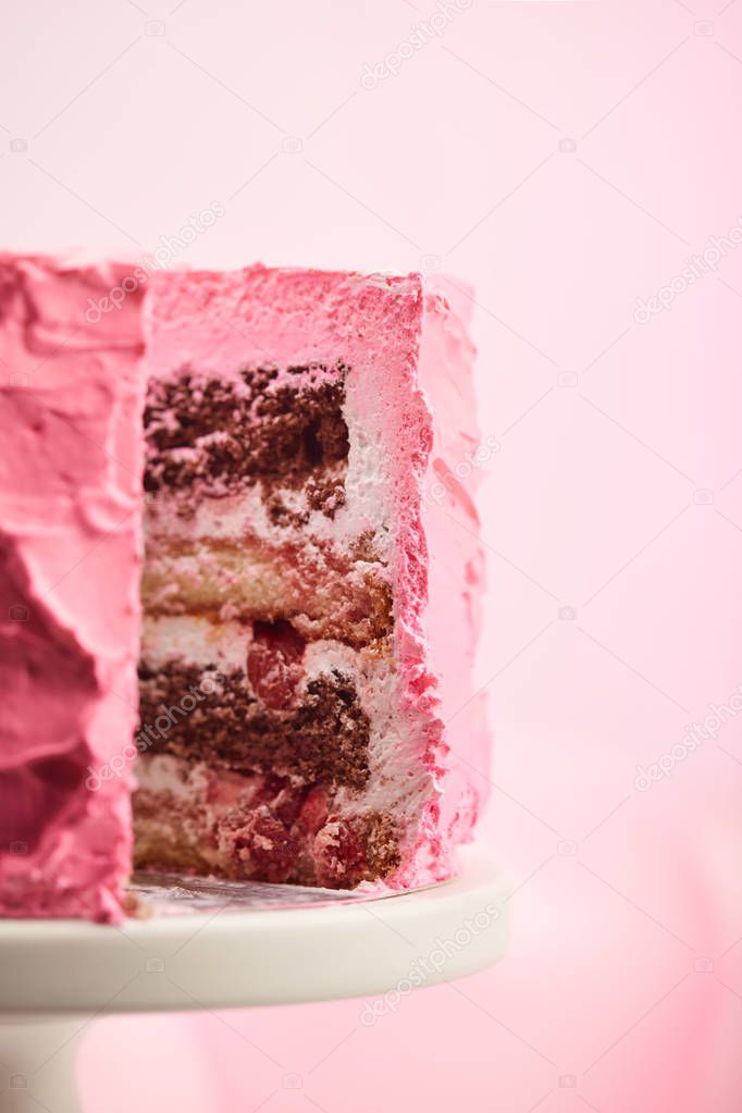 close up of cut pink birthday cake on cake stand on pink 