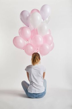 arkadan görünüşü oturan ve beyaz üzerine pembe hava balonları tutarak rahat kıyafetler kız