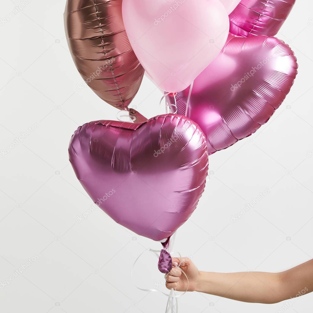 partial view of girl holding heart-shaped pink air balloons isolated on white