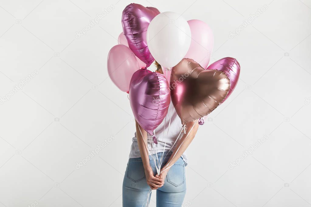 back view of girl in denim holding heart-shaped pink air balloons isolated on white
