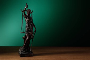 koyu yeşil zemin üzerine ahşap yüzeyde adaletin terazisi ile bronz heykelciği
