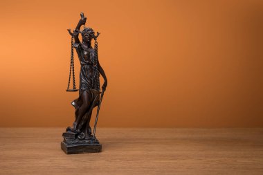 Turuncu zemin üzerine ahşap masa üzerinde adaletin terazisi ile bronz heykelciği