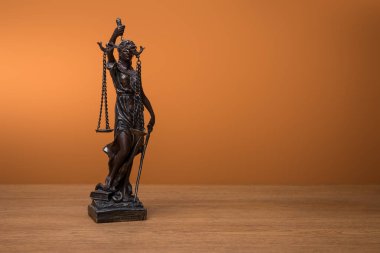 bronze statuette with scales of justice on wooden table on orange background clipart