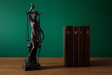 bronze statuette with scales of justice and volumes of brown books on wooden table on dark green background clipart