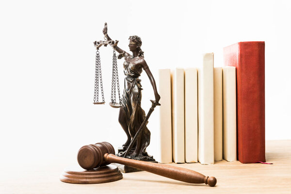 figurine with scales of justice, brown gavel and books on wooden table isolated on white