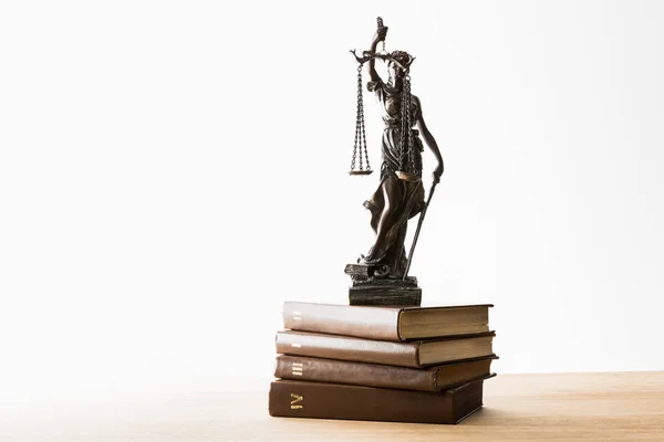 bronze figurine with scales of justice on pile of brown books on wooden table isolated on white