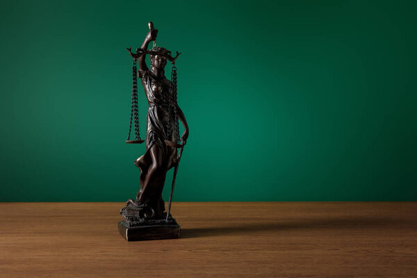 bronze statuette with scales of justice on wooden table on dark green background