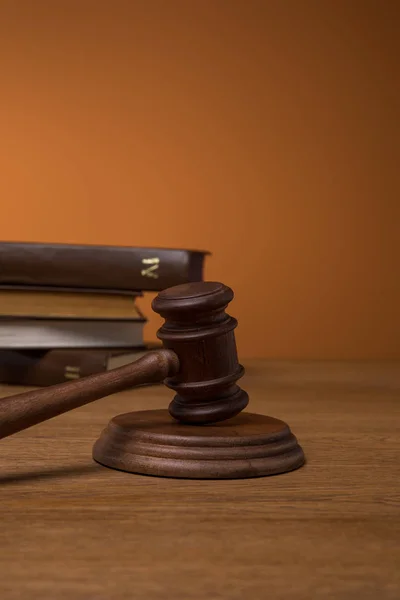selective focus of volumes of brown books in leather covers and gavel on wooden table on dark orange background