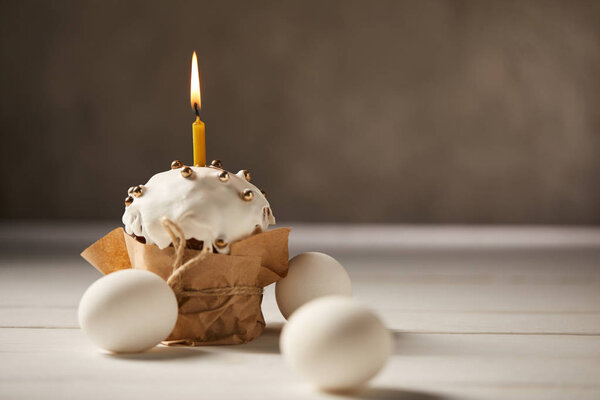 traditional easter cake with burning candle and chicken eggs on white table with copy space