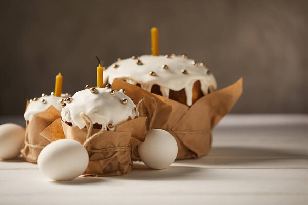 traditional easter cakes with candles and chicken eggs on white surface