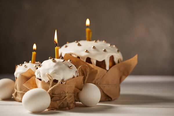 traditional easter cakes with burning candles and chicken eggs on white surface