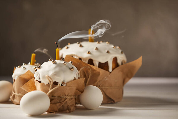 chicken eggs and traditional easter cakes with candles, sprinkles and frosting on white table 