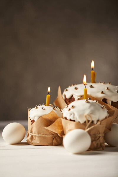 delicious easter cakes with burning candles and chicken eggs on white table