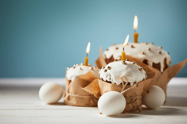 selective focus of delicious easter cakes with candles and chicken eggs on turquoise 