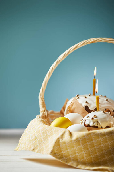 easter cakes with chicken eggs and napkin in wicker basket on turquoise with copy space