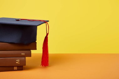 Academic cap and brown books on orange surface isolated on yellow clipart