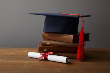 Diploma, akademik kap ve gri üzerinde ahşap yüzeydeki kitaplar