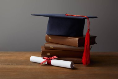 Diploma, academic cap and books on wooden surface on grey clipart