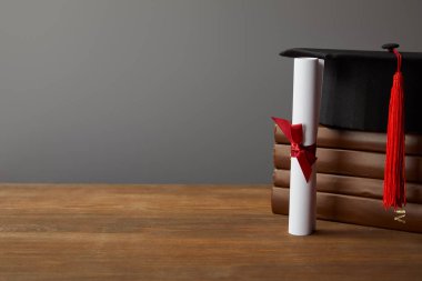 Diploma, akademik kap ve ahşap yüzeyde kitap gri üzerinde izole