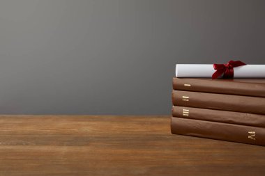Gri üzerinde ahşap yüzeyde kırmızı kurdele ile kahverengi kitaplar ve diploma