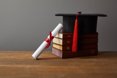 Diploma, akademik kap ve ahşap yüzeyde kitap gri üzerinde izole