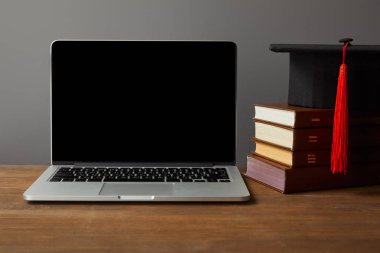 Boş ekran ile Laptop, gri üzerinde izole ahşap yüzey üzerinde kitaplar ve akademik kap