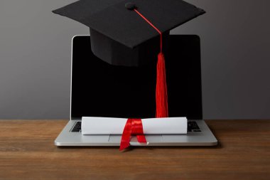 Laptop with blank screen, diploma and academic cap with red tassel on grey clipart