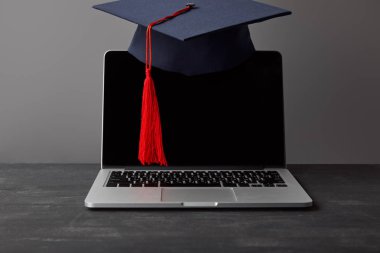 Gri üzerinde kırmızı püskül ile boş ekran ve akademik kap ile Laptop