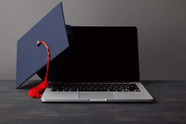 Gri üzerinde kırmızı püskül ile boş ekran ve akademik kap ile Laptop