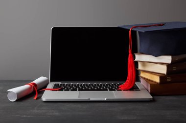Boş ekran, diploma, kitap ve kırmızı püskül ile akademik kap ile Laptop gri izole