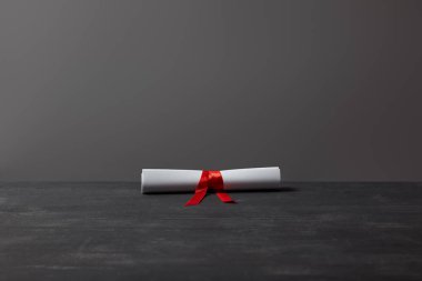 Gri üzerinde koyu dokulu yüzeyde kırmızı şerit ile diploma