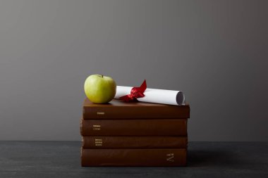 Kahverengi kitaplar, gri üzerinde dokulu yüzeyde kurdele ve yeşil elma ile diploma