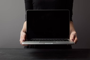 Gri üzerinde boş ekran ile kadın tutan laptop kısmi görünümü