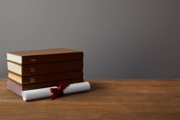 Brown books and diploma with red ribbon on wooden surface on grey