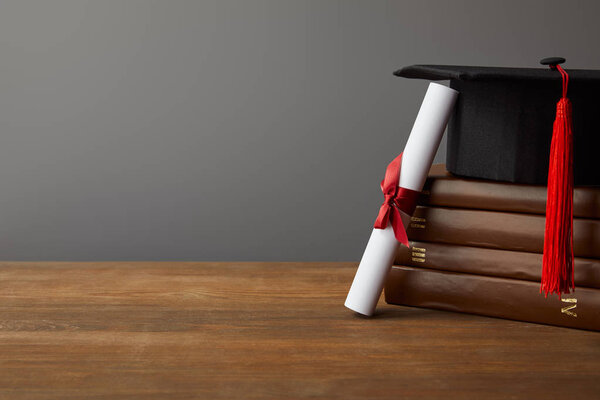 Diploma, academic cap and books on wooden surface isolated on grey