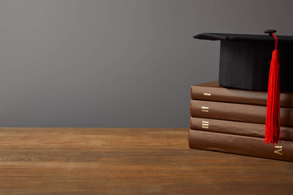 Brown books and academic cap on wooden surface isolated on grey