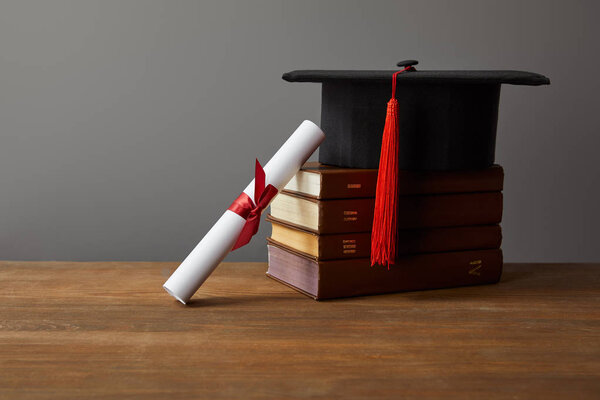 Diploma, academic cap and books on wooden surface isolated on grey