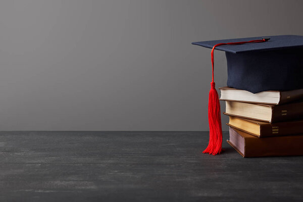 Brown books and academic cap with red tassel isolated on grey