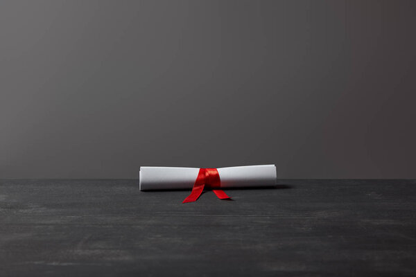 Diploma with red ribbon on dark textured surface on grey