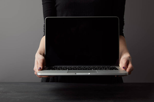 Partial view of woman holding laptop with blank screen on grey
