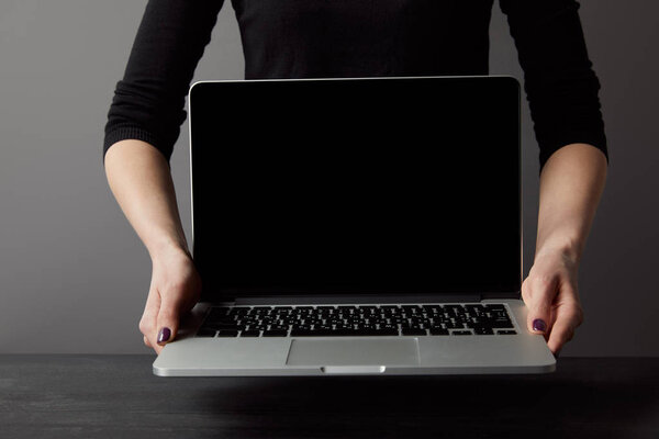 Partial view of woman holding laptop with blank screen on grey