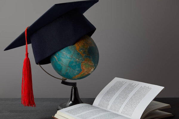 Globe, academic cap with red tassel and open book on texture surface on grey